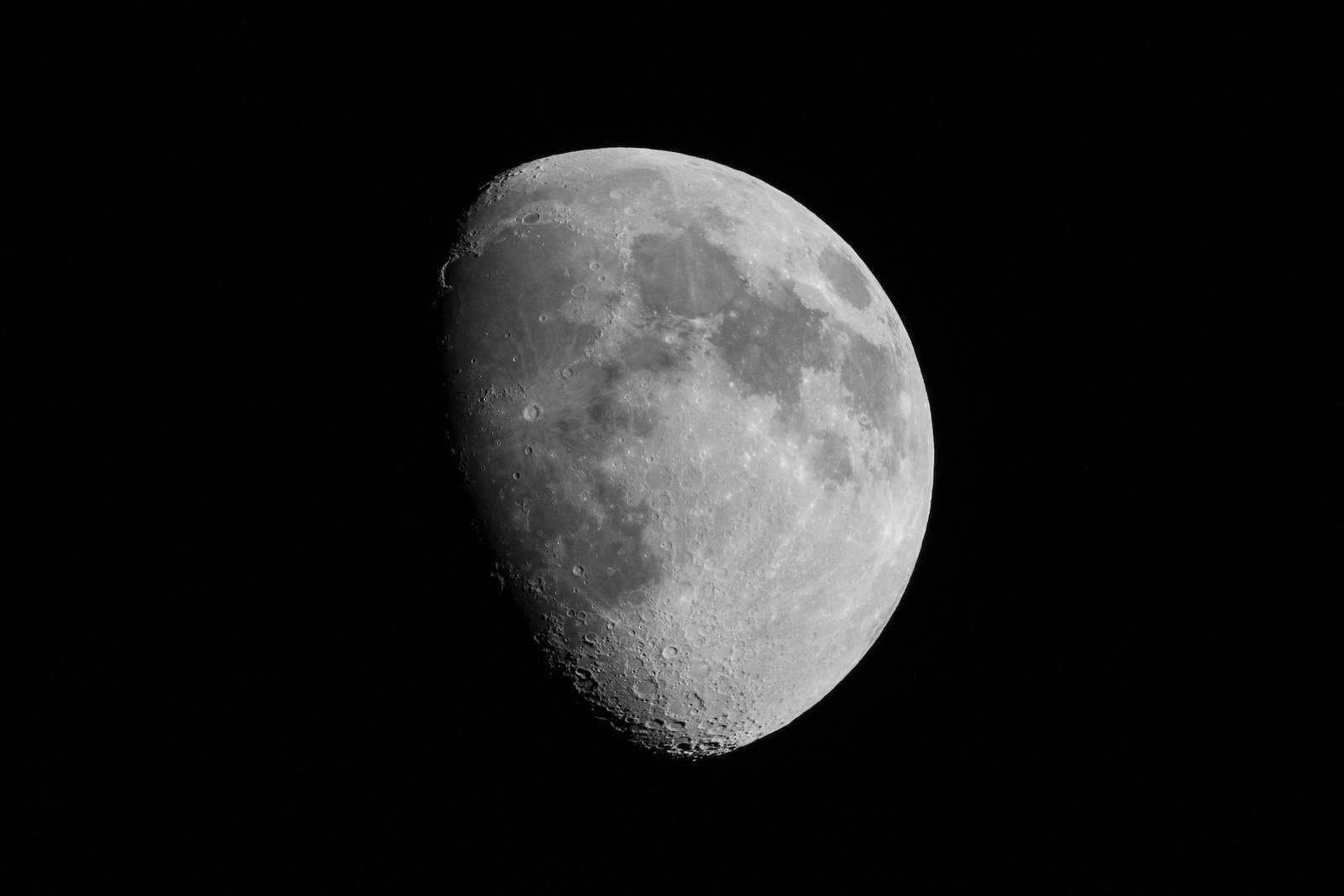 telescopic image of grey colored circular moon in waxing gibbous phase, with dark spots on it